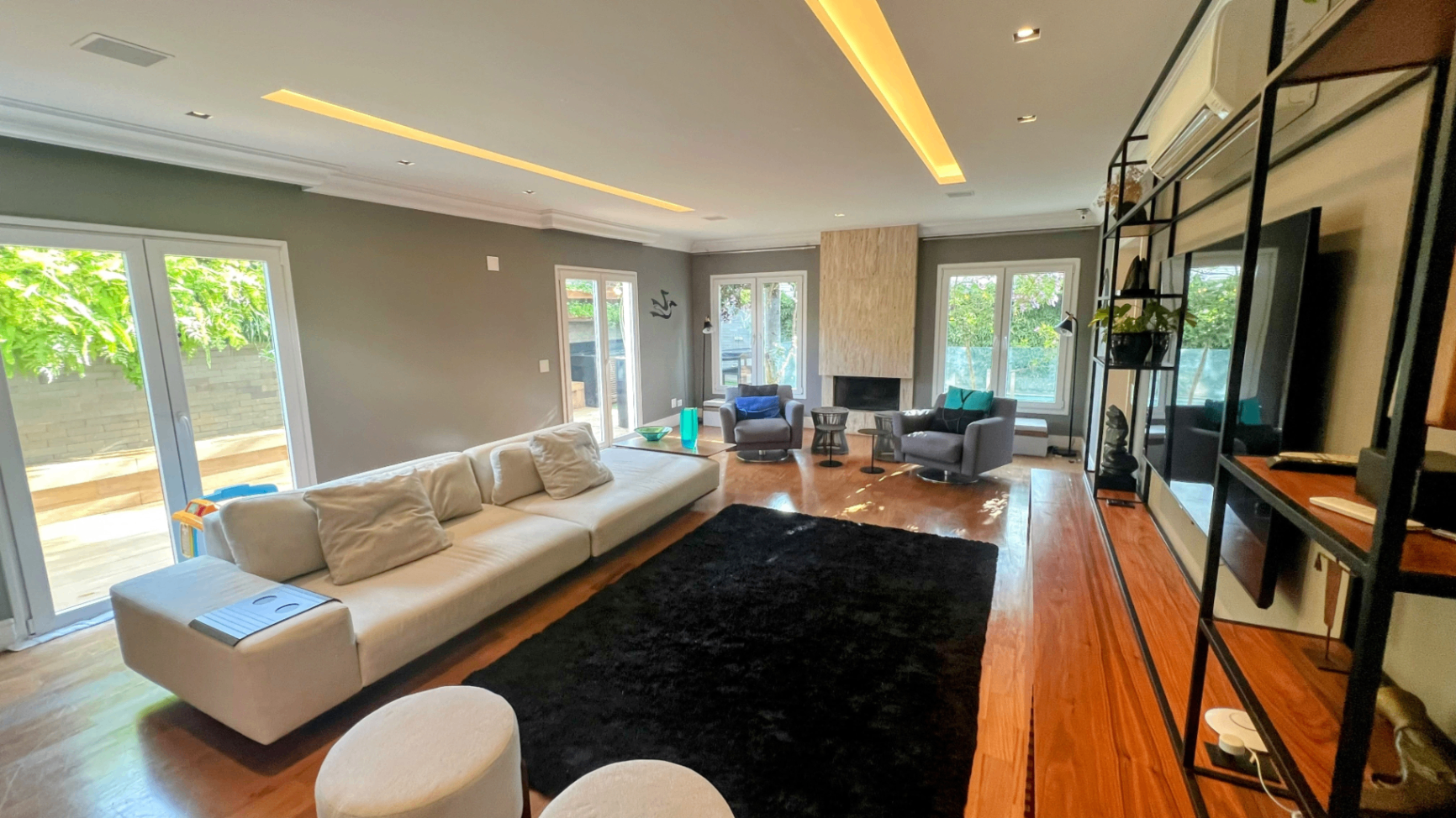 Living amplo com sofá branco, tapete preto e painel de TV integrado à marcenaria