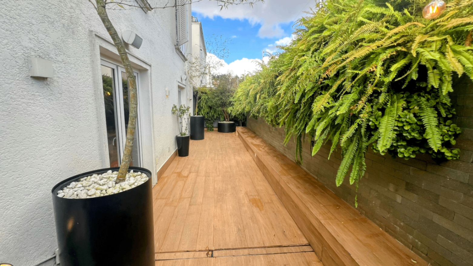 Deck externo com sofá, jardim vertical e passagem para a piscina