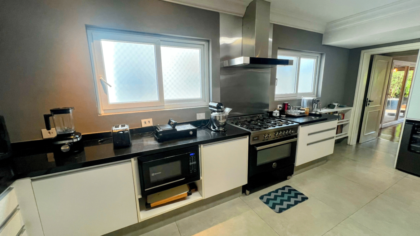 Cozinha com fogão gourmet de seis bocas, coifa em inox e bancada preta