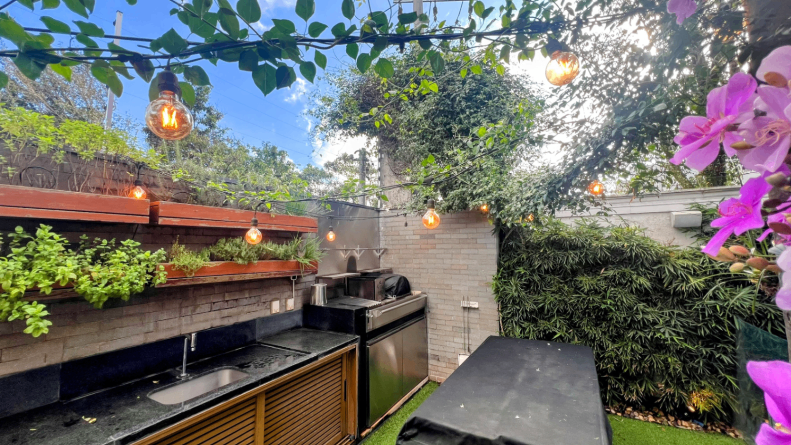Pergolado da área gourmet com iluminação decorativa e horta ao lado