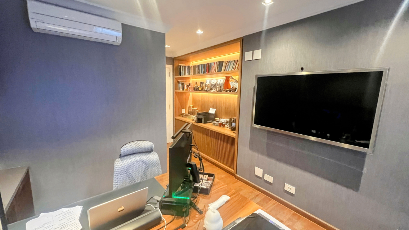 Sala multiuso com painel de TV, ar-condicionado e marcenaria em madeira