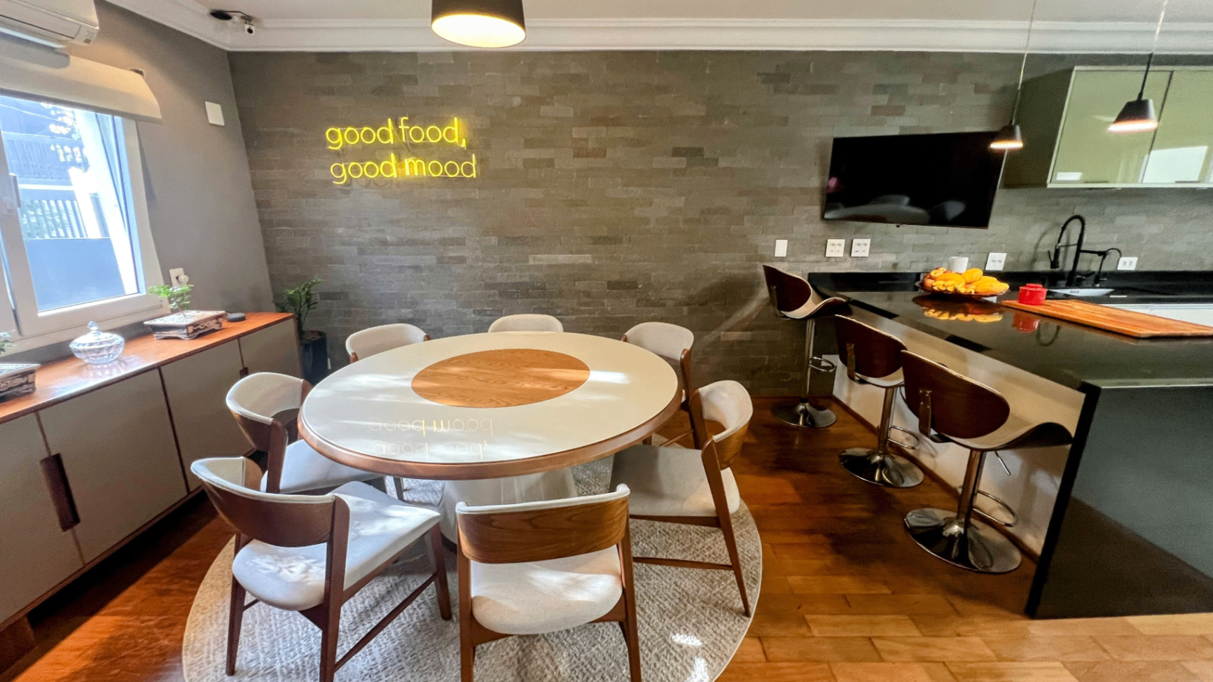 Sala de jantar com mesa redonda, luminária pendente e letreiro decorativo ao fundo