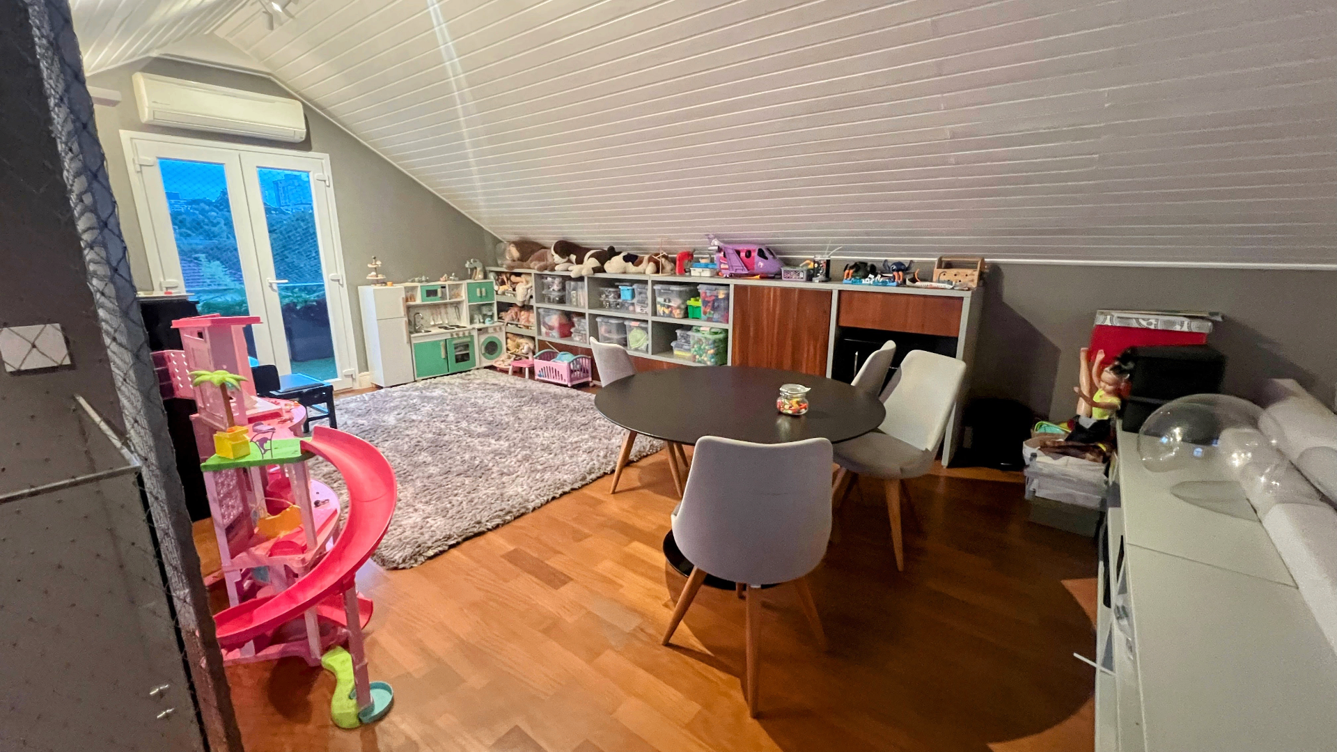 Sótão como brinquedoteca com mesa, tapete felpudo e brinquedos organizados