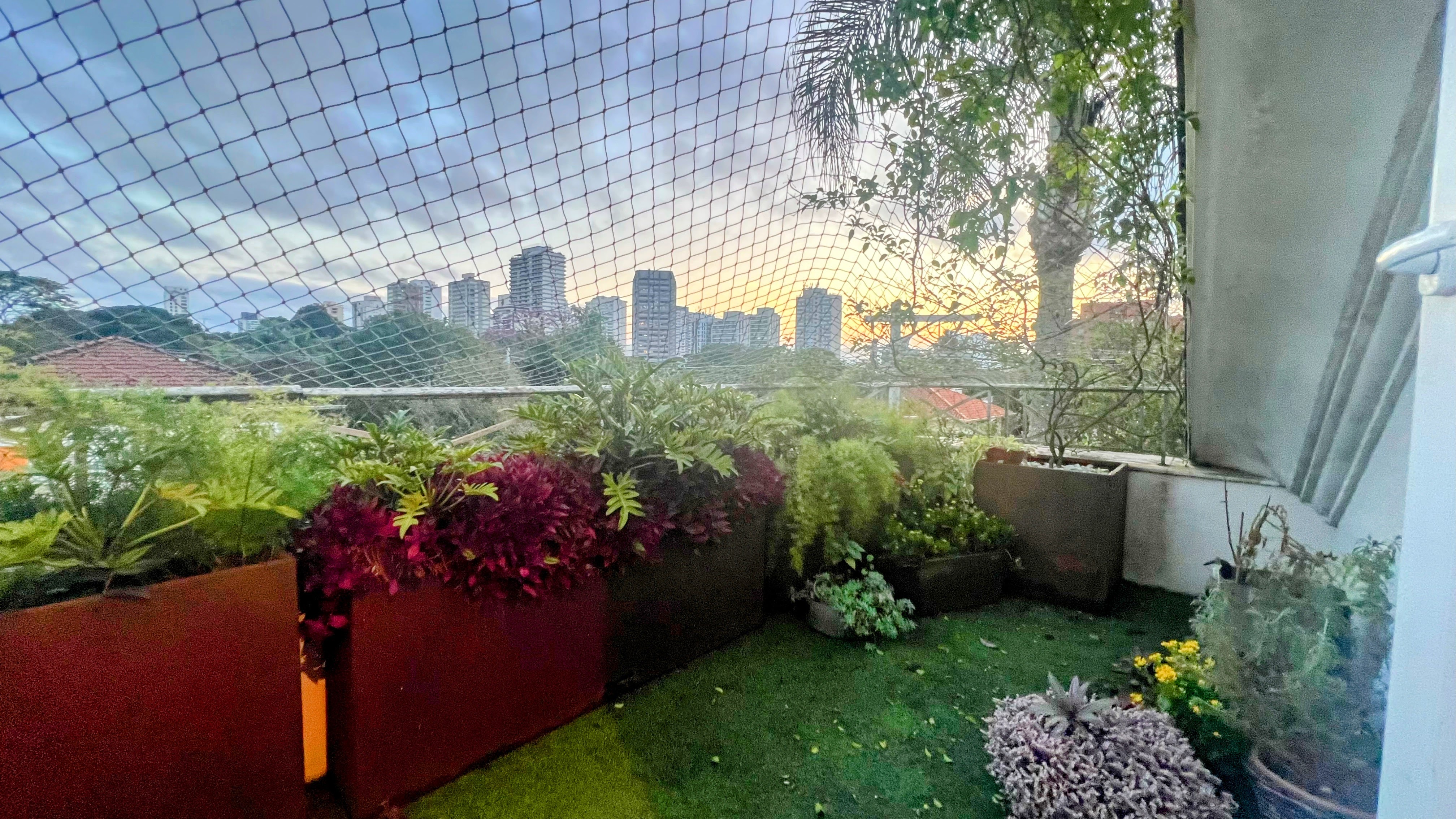Terraço com jardineiras e vista aberta do bairro ao entardecer