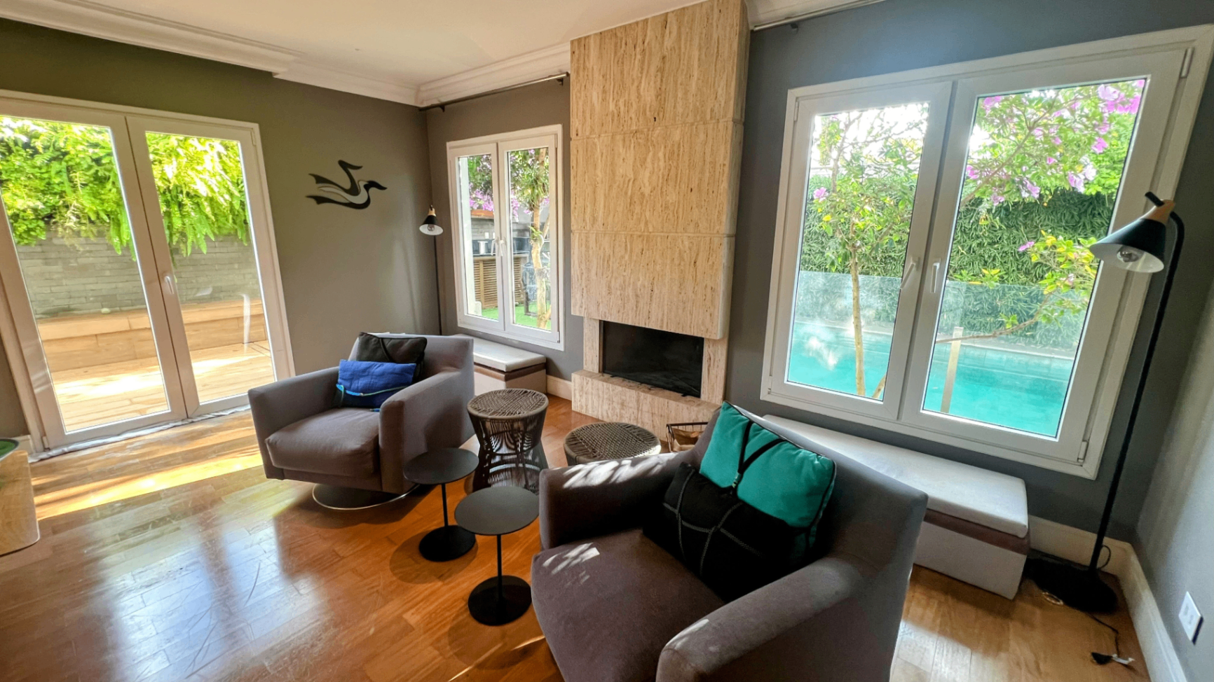 Sala de estar com lareira em pedra, poltronas cinza e janelas para o jardim