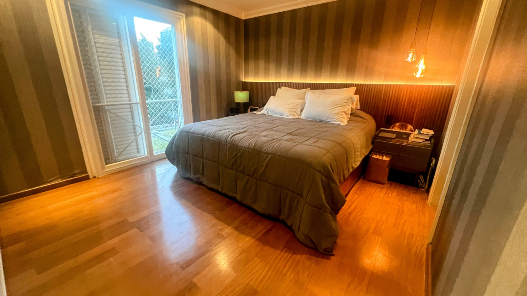 Suíte de casal com cama king, cabeceira ripada e iluminação quente