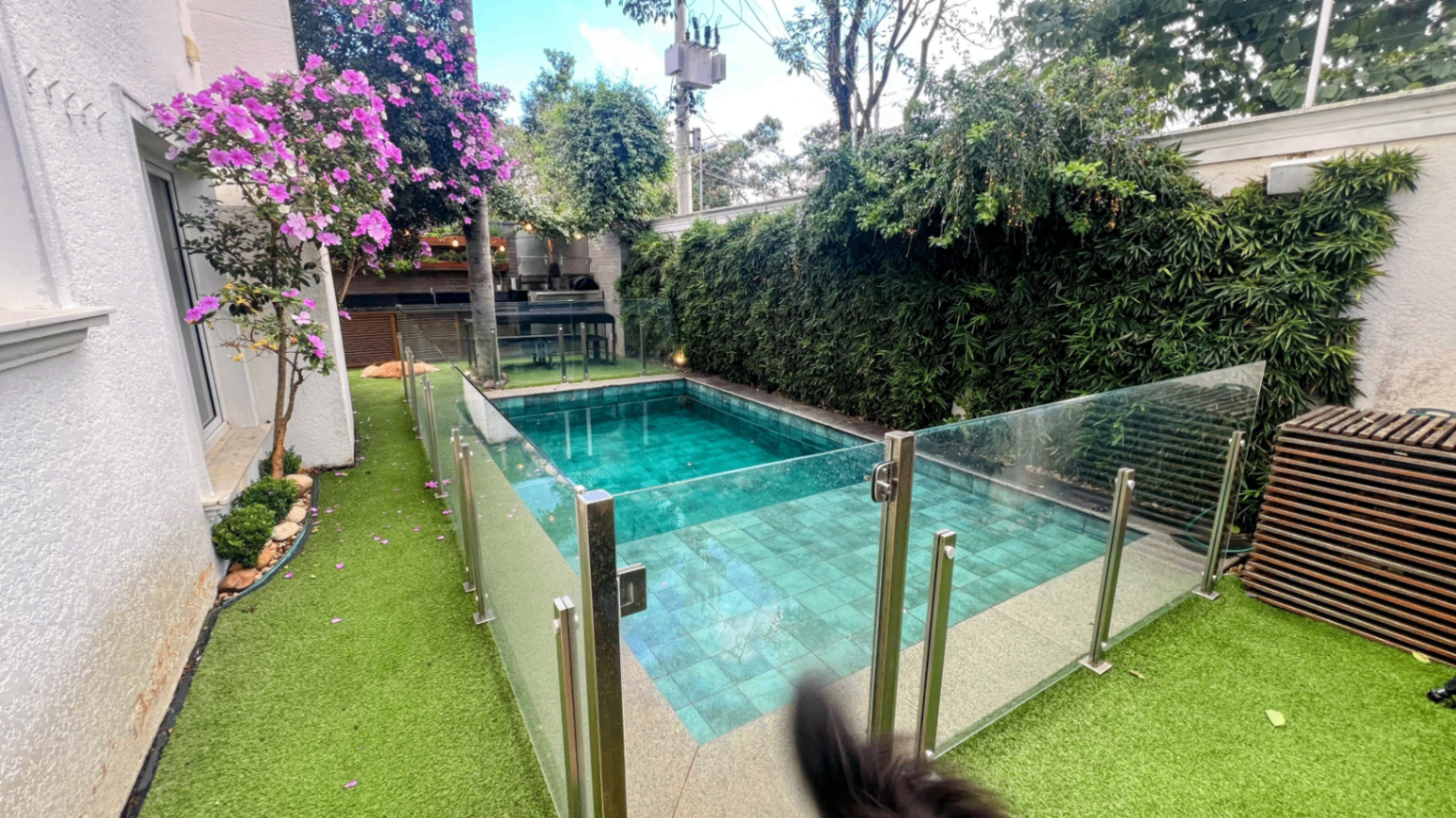 Piscina lateral com cerca de vidro, deck de madeira e jardim vertical