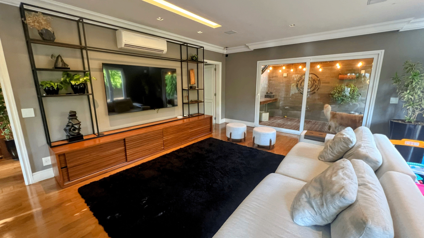 Sala de TV com painel de marcenaria, estante e integração com o jardim