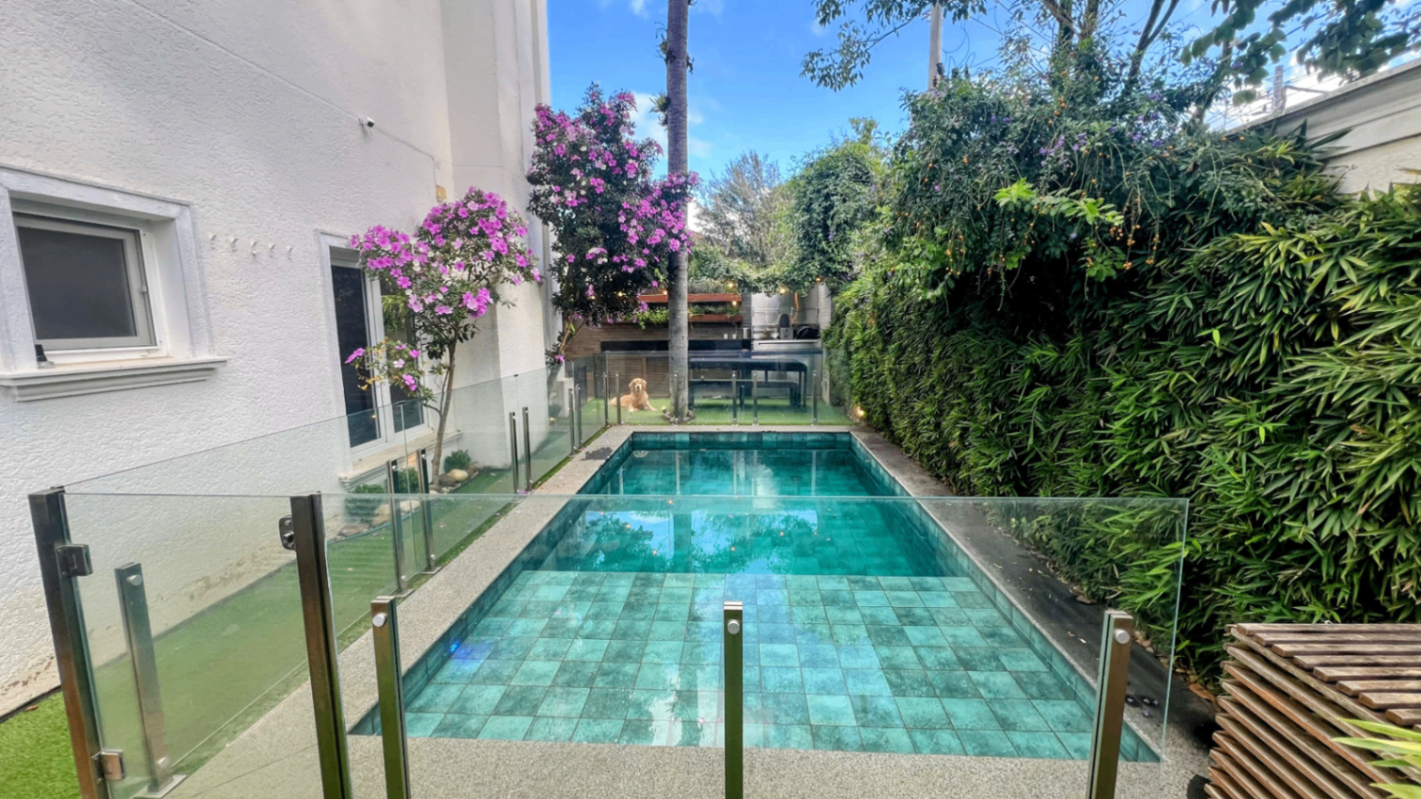 Piscina com paisagismo tropical, buganvília em flor e mesa lateral
