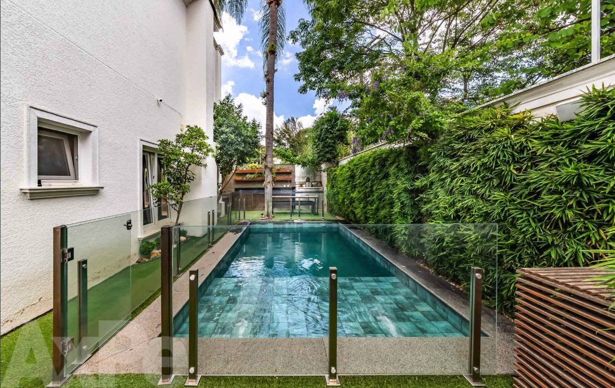 Piscina lateral com cerca de vidro e jardim tropical